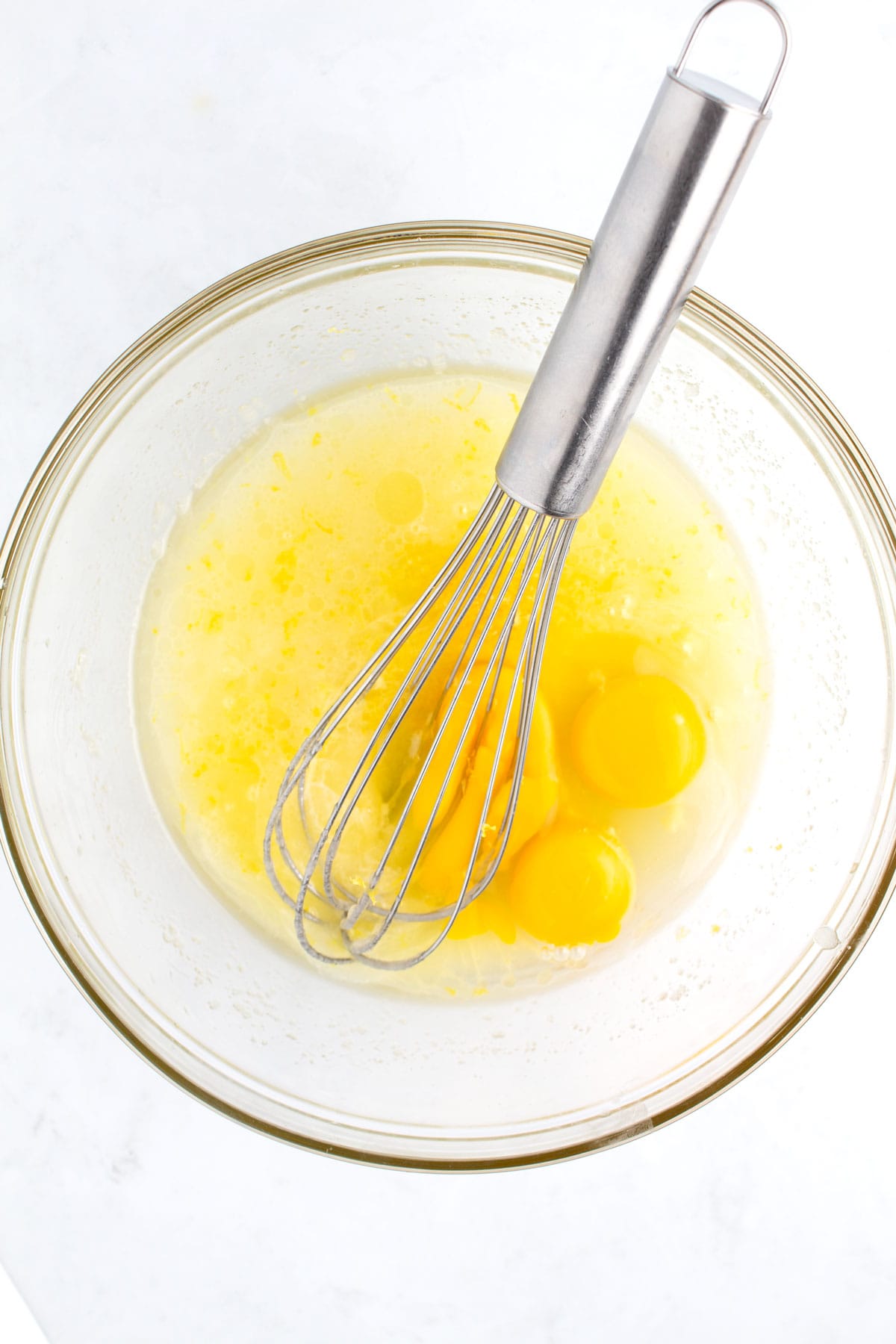 A glass bowl of melted butter and eggs with a whisk sitting in the bowl.