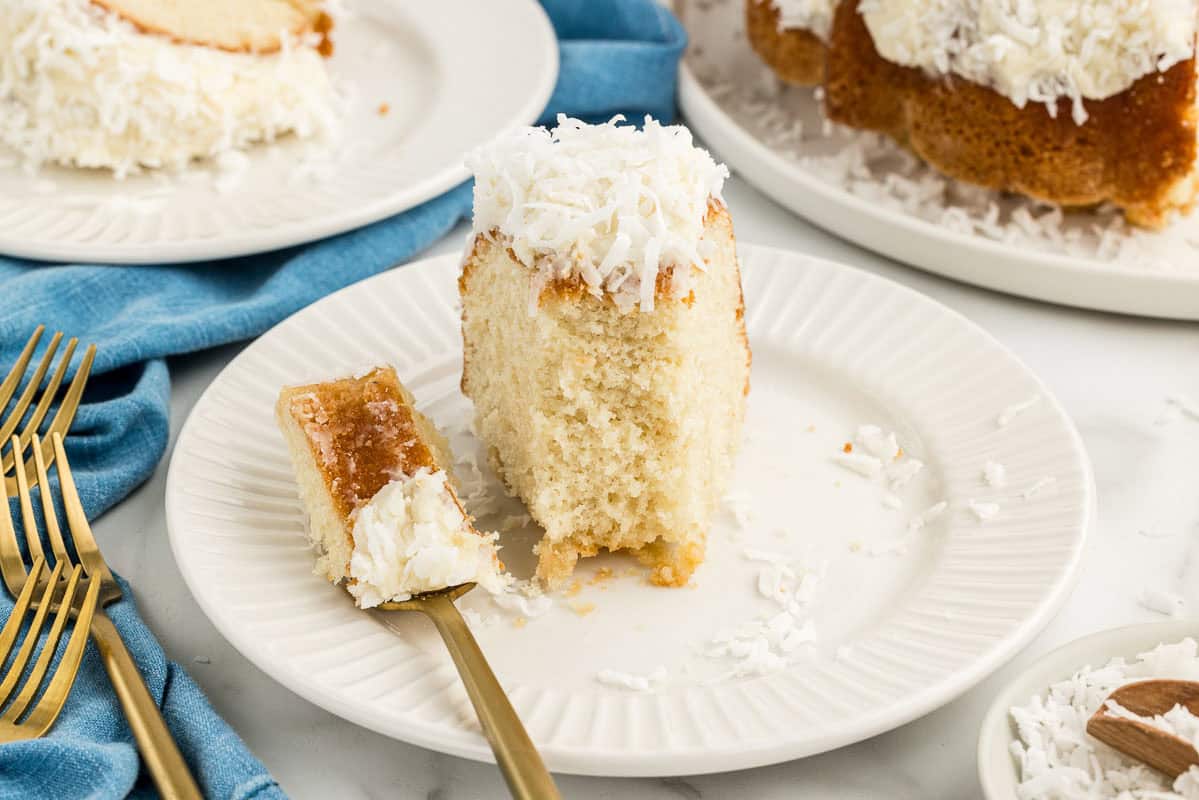 Slice of coconut Bundt cake on a plate with a bite taken out of it and put on a fork next to it.