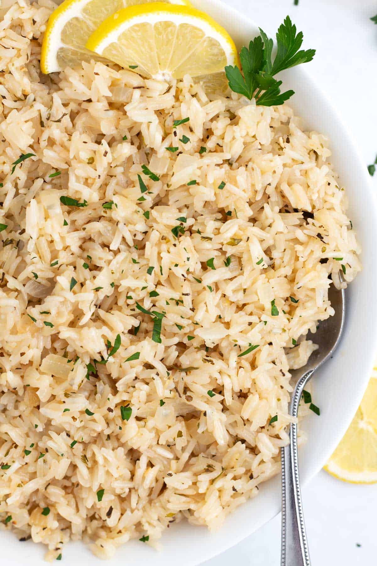 A bowl of moist lemon rice with a spoon in it topped with lemon slices.