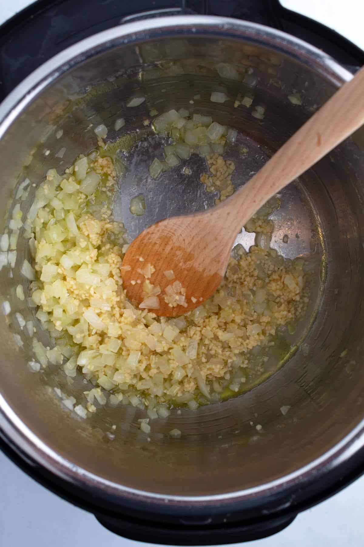 Garlic and onions cooking in a pot with a wooden spoon.