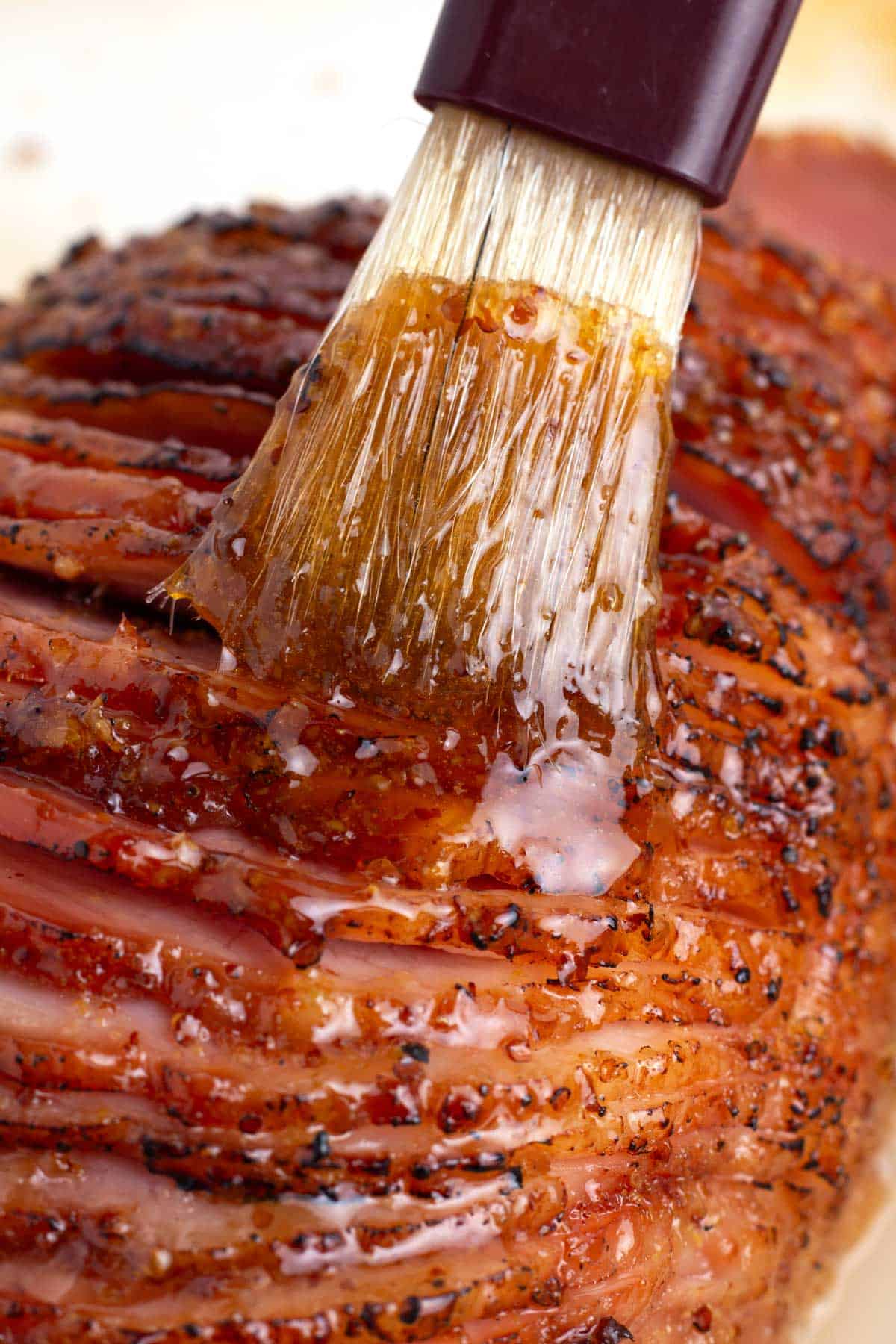 A sliced ham getting brushed with 3 ingredient glaze.