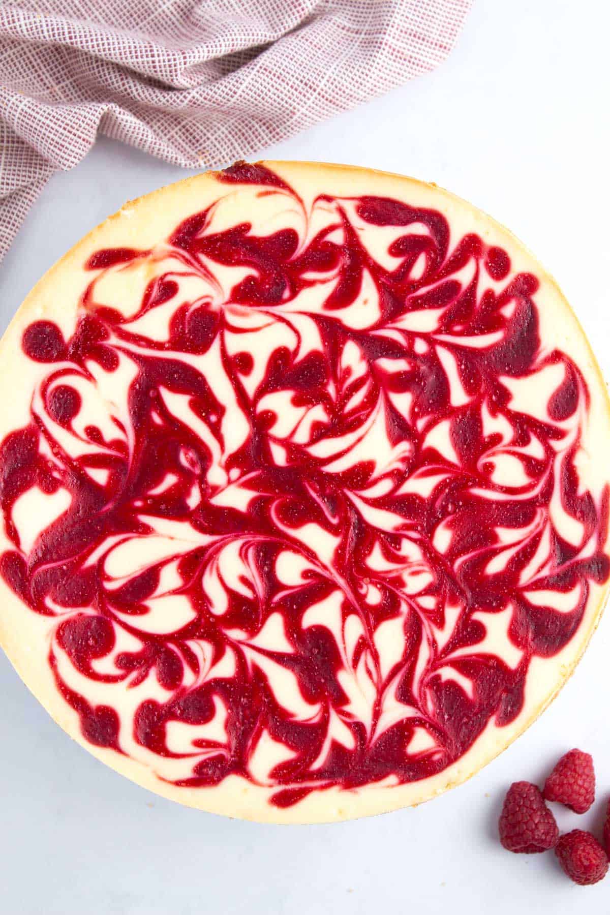 Baked and swirled cheesecake next to a pile of raspberries.