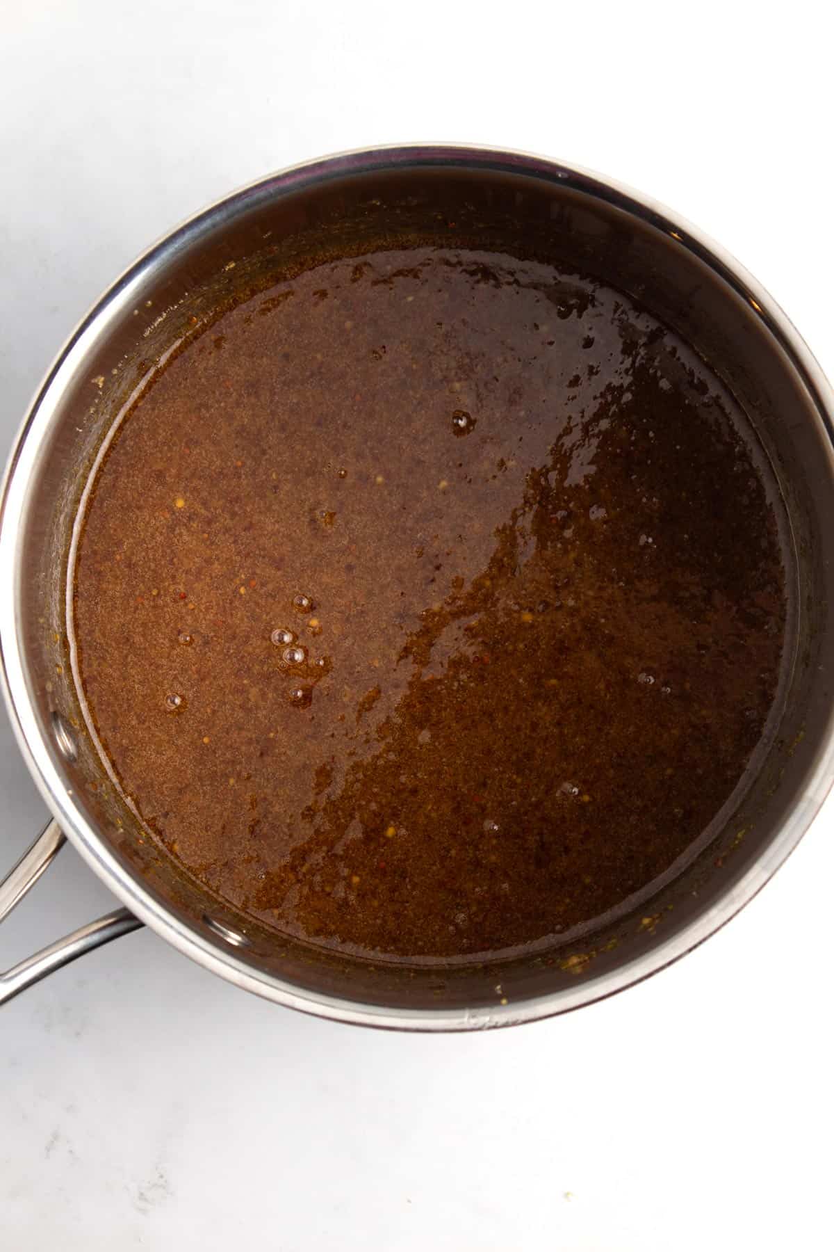 A saucepan containing bubbling ham glaze on a white countertop.