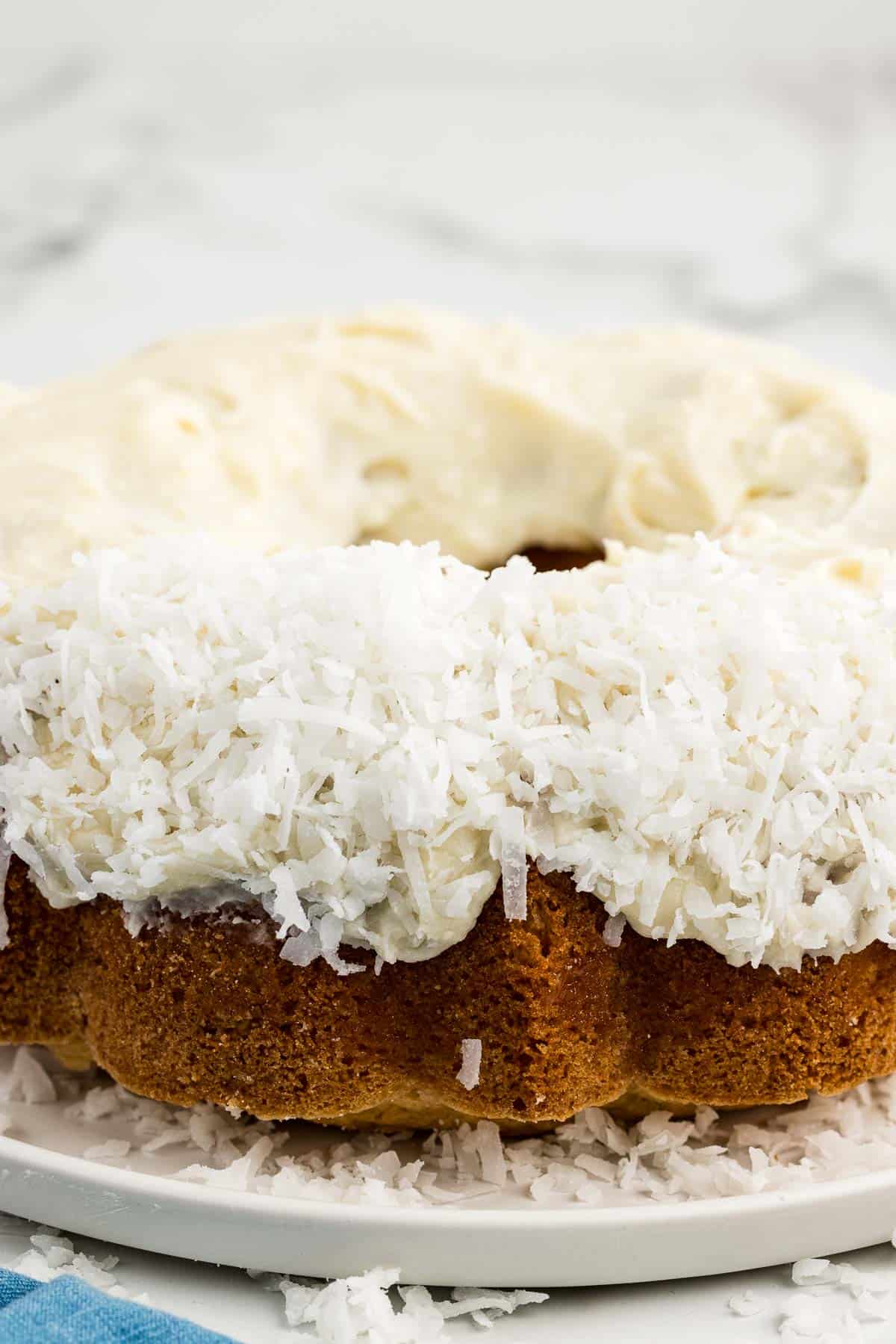 Bundt cake topped with shredded coconut flakes on a white platter.