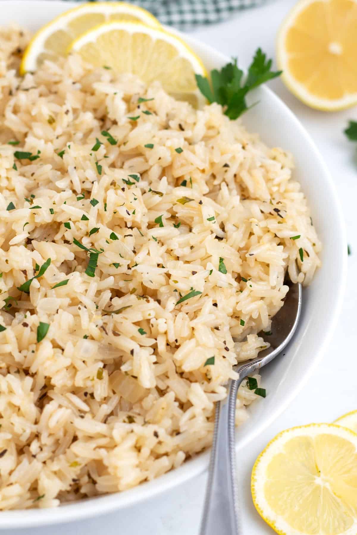a white dish of rice surrounded by sliced lemons and a spoon leaning against the rim.