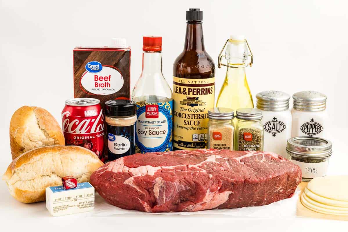 Bread, a stick of butter, a can of Coca Cola, beef broth, chuck roast, garlic powder, soy sauce, Worcestershire sauce, onion powder, oregano leaves, oil, salt and pepper, thyme, and cheese on a countertop.