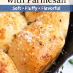 Buttery dinner rolls with garlic and parmesan in a cast iron pan with a graphic overlay.