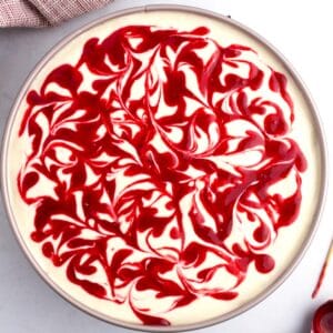 Batter in a round pan with swirled raspberry syrup on top.