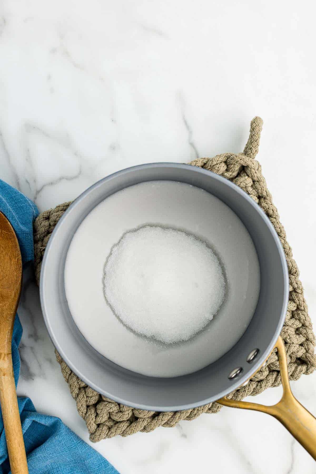 A small saucepan on a hot pad with coconut syrup ingredients in it.
