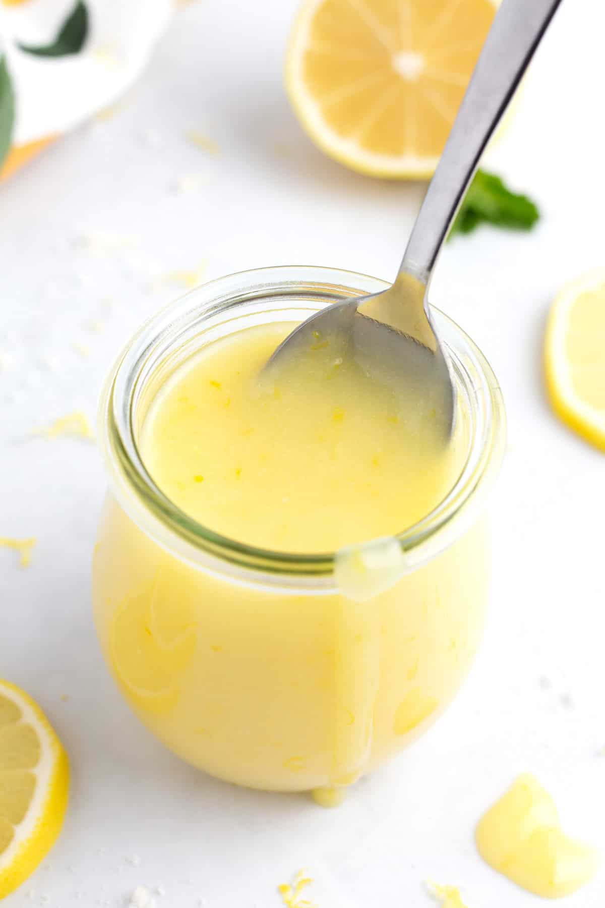 A spoon scooping lemon curd out of a small jar.