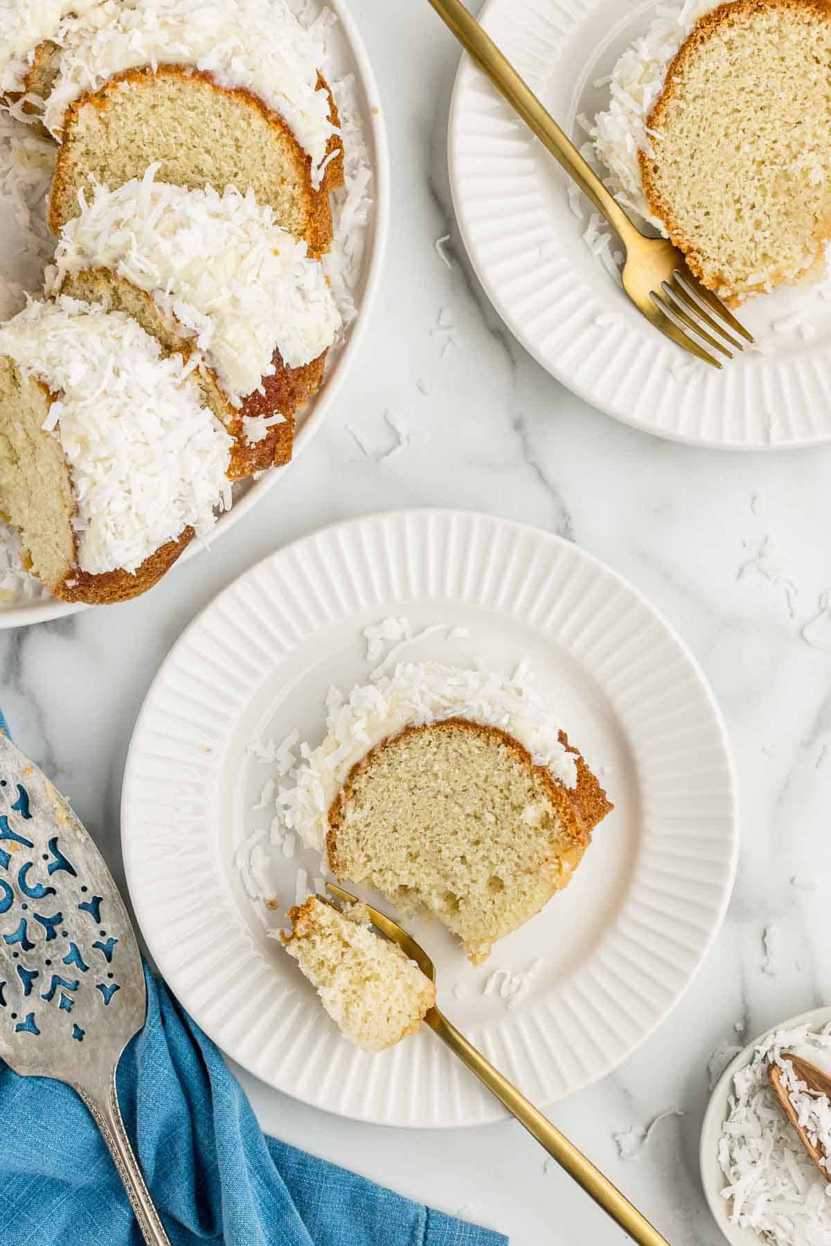 Two plates with slices of coconut Bundt cake with forks next to a platter with the rest of the sliced cake.