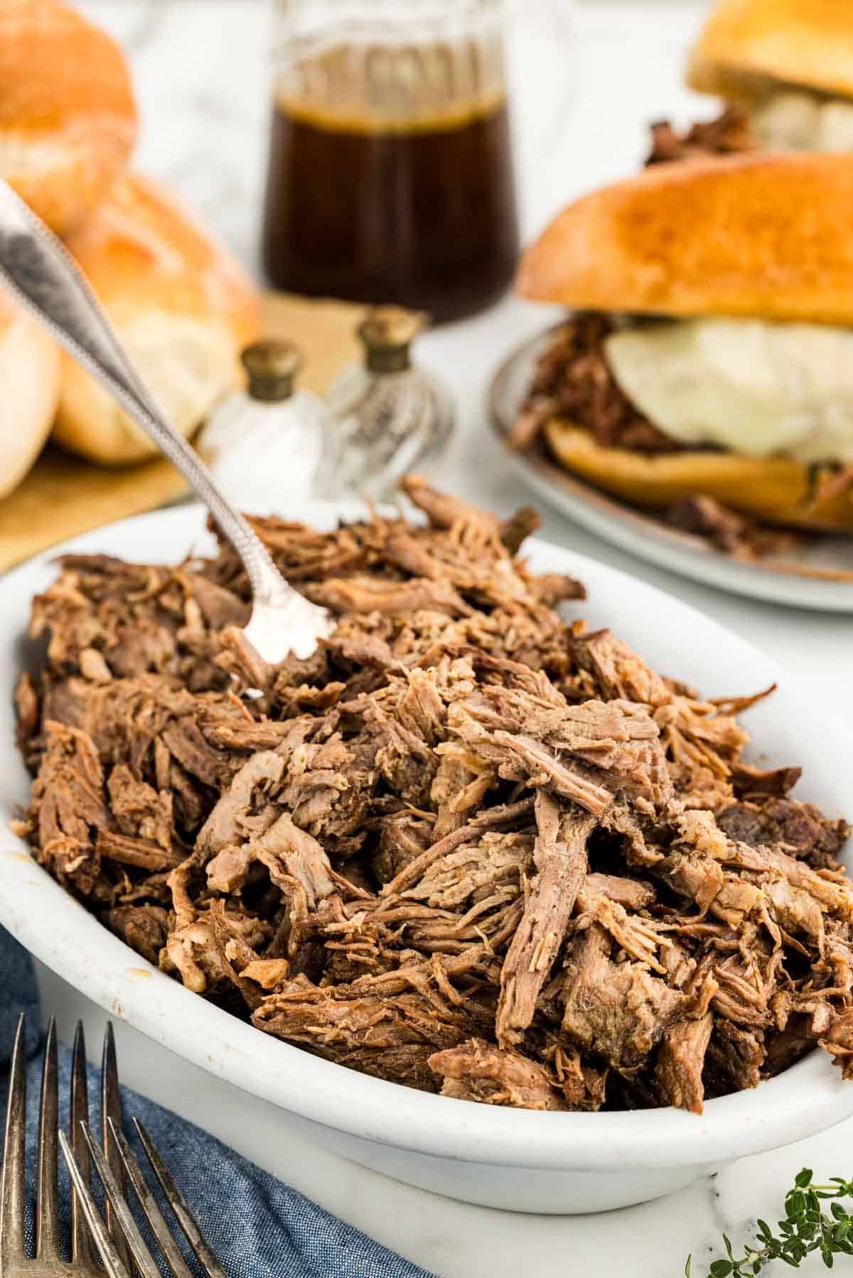 A white dish of meat with a fork sticking out of it in front of sandwich ingredients.