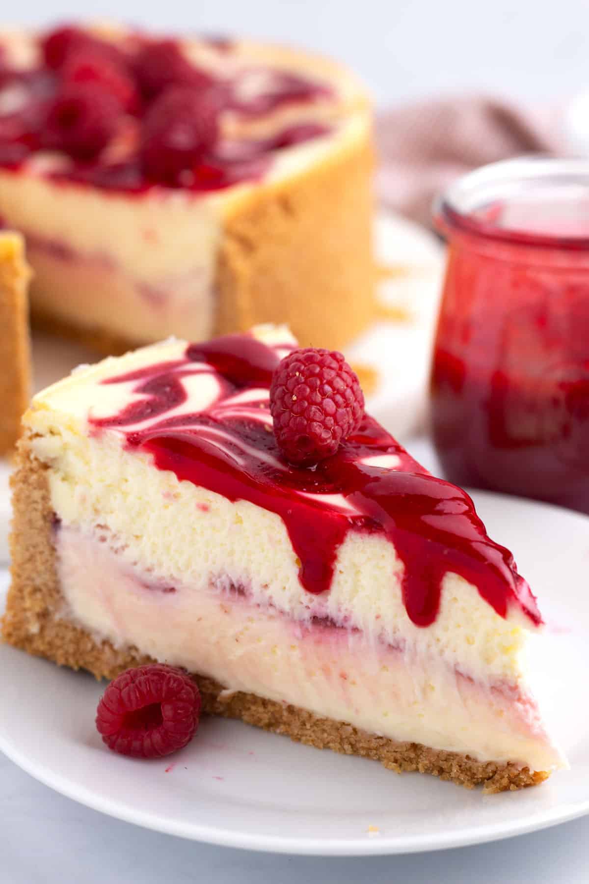 A slice of creamy cheesecake on a small plate topped with raspberry sauce.