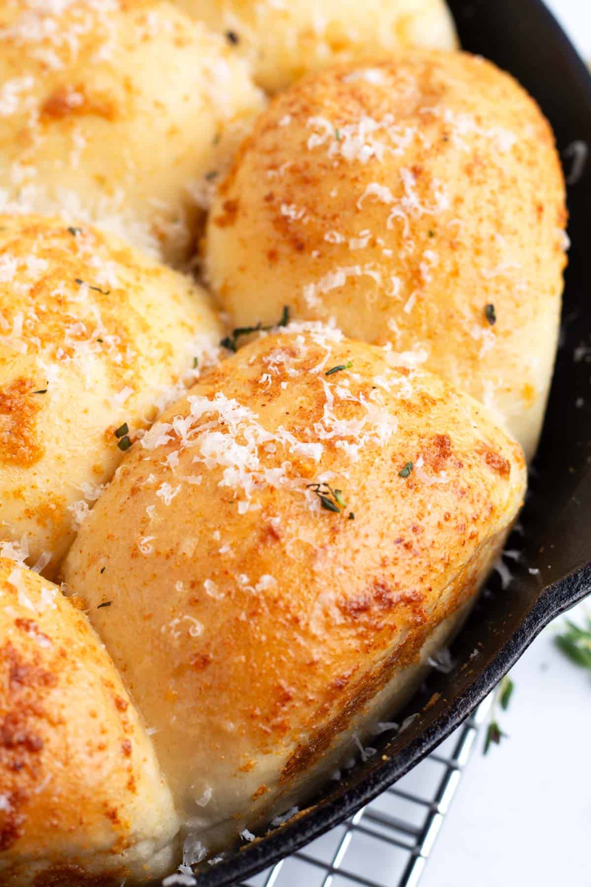 Buttery garlic Rhodes rolls with parmesan in a cast iron pan on top of a cooling rack.