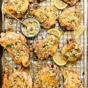 Delicious chicken thighs cooling on a rack with a dish of lemon parmesan topping nestled between them.