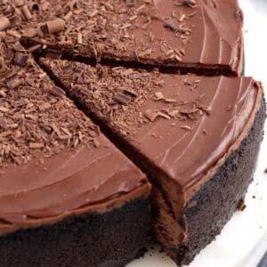 Slice of ganache covered chocolate cheesecake with Oreo crust coming out of whole dessert.