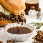 A chuck roast sandwich over a small dish dripping with French dip.
