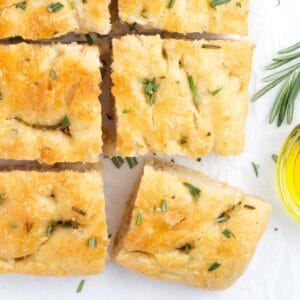 A loaf of sliced focaccia squares sprinkled with rosemary.