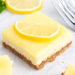 A cheesecake lemon square with fresh icing next to a fork.