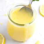 A small glass container full of lemon curd with a spoon dipped into the top.
