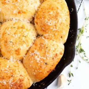 Parmesan garlic Rhodes rolls in a cast iron skillet with a piece of garlic next to it.