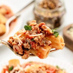 A bite of sausage and pasta dinner on a fork over a white dish.