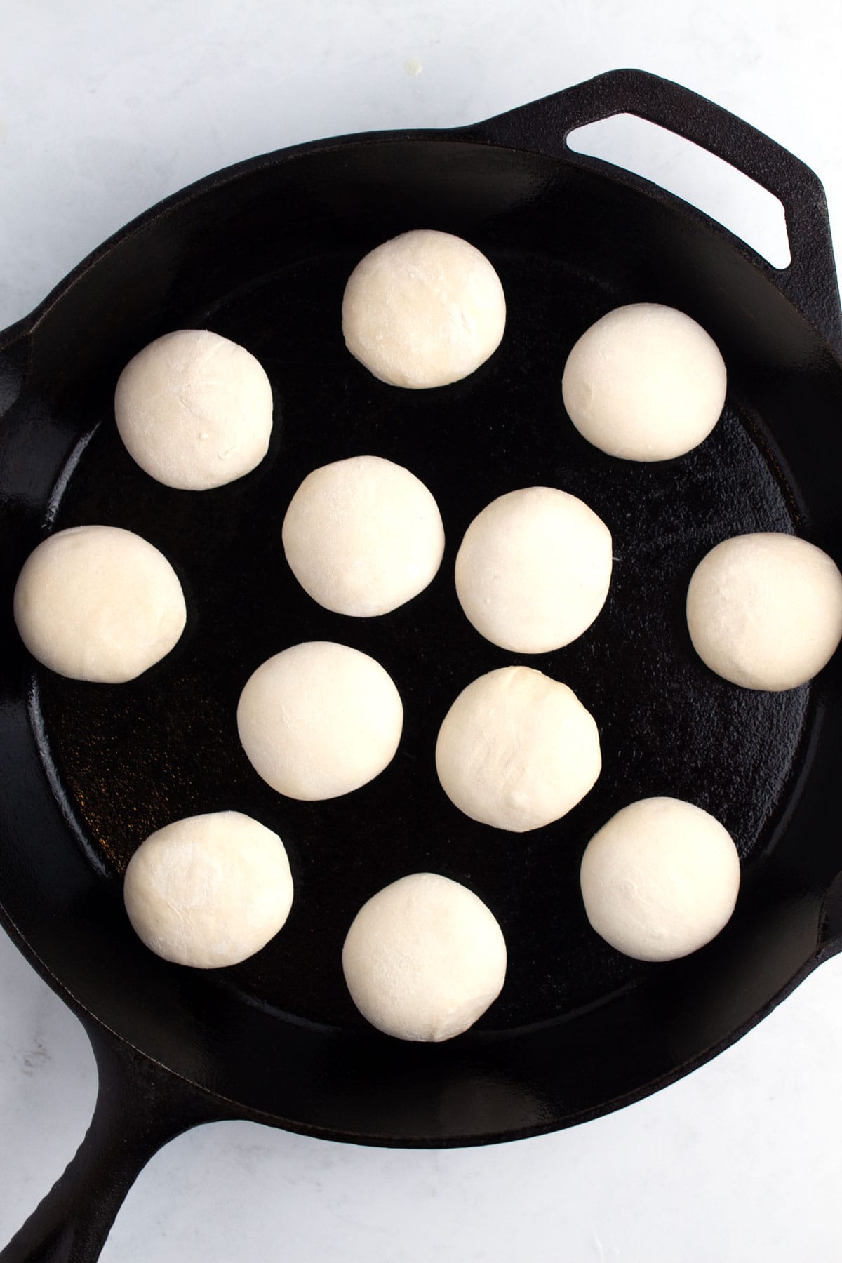 A cast iron skillet with rolls of dough placed apart from each other.