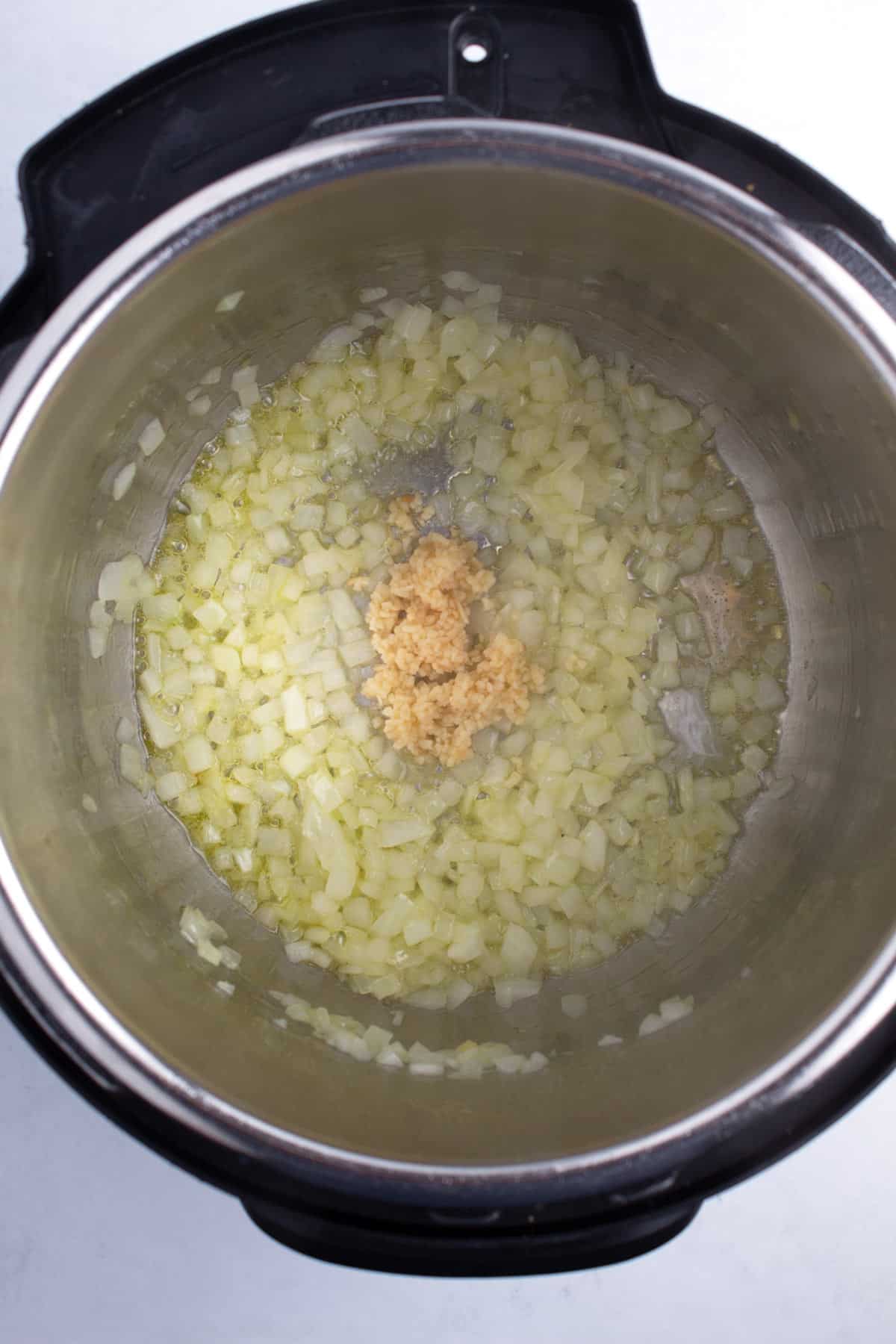 A large pot of simmering onions and garlic on a white counter.