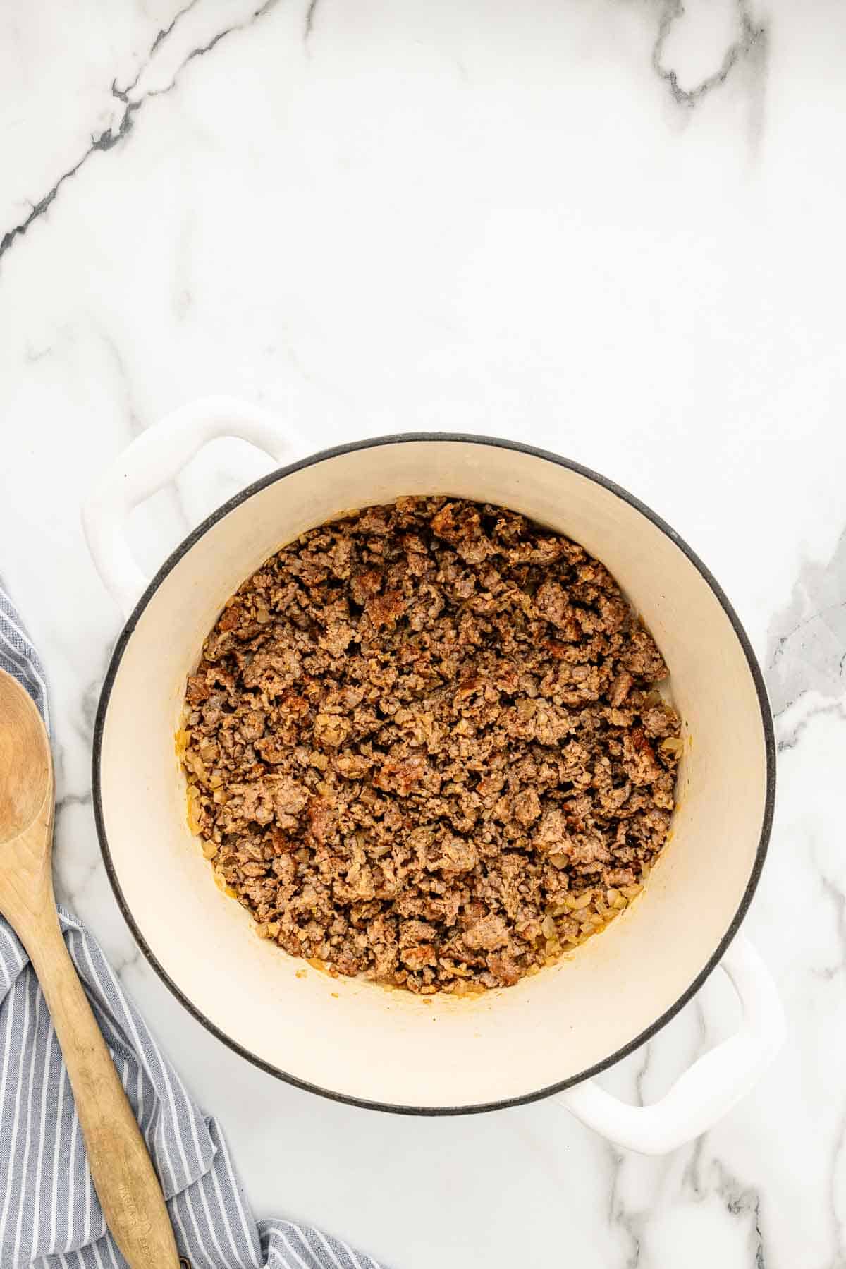 Ground sausage in a pot with a cooking spoon next to it.