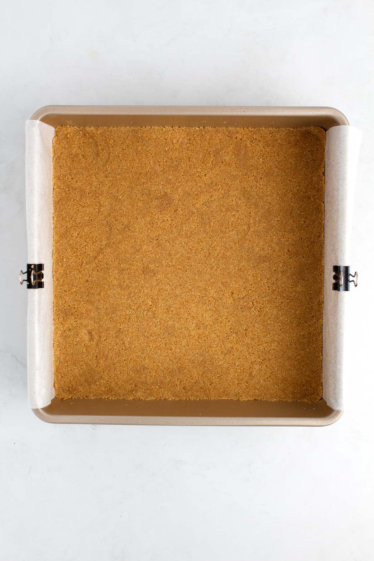 A square sheet pan of graham cracker crust on a white counter.