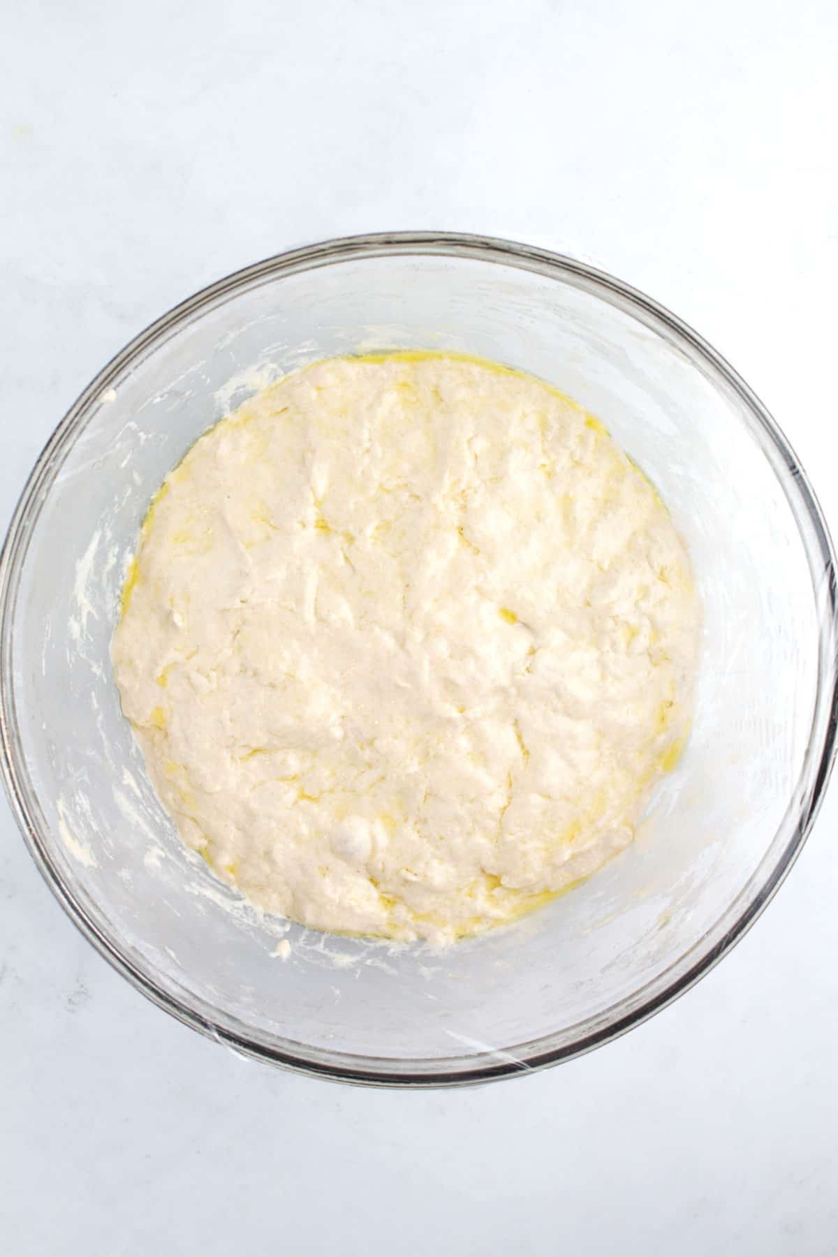 A mixing bowl full of dough and oil covered with plastic wrap.