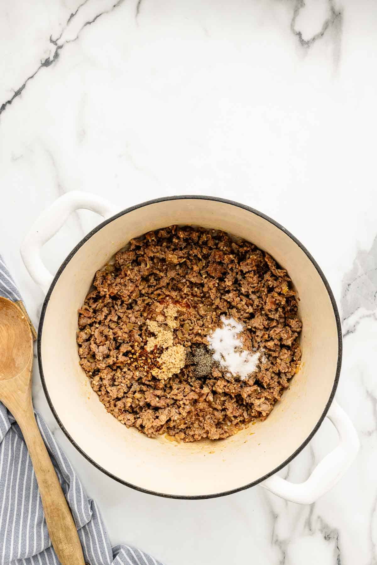 Ground meat with seasonings in a large pot on a marble counter.