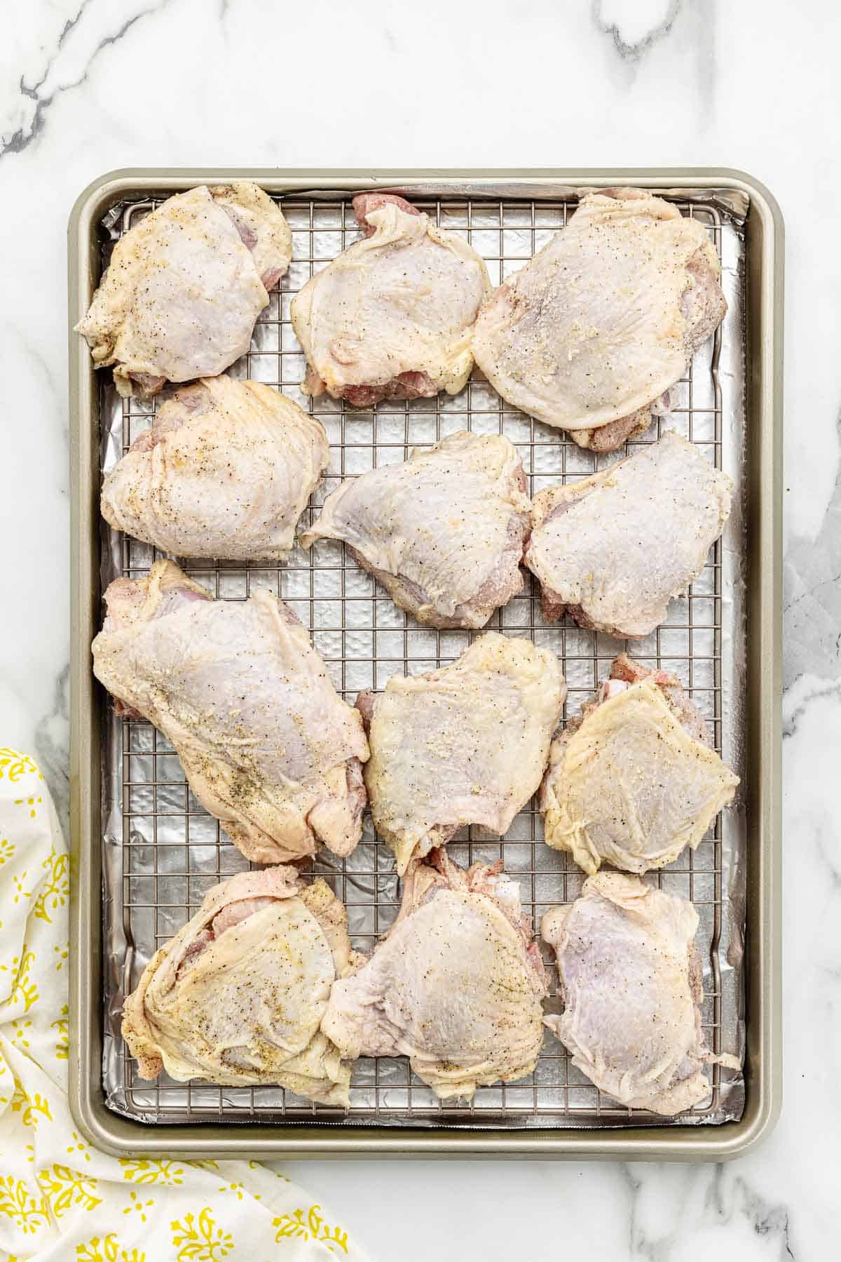 A pan holding a rack with uncooked chicken thighs on it.
