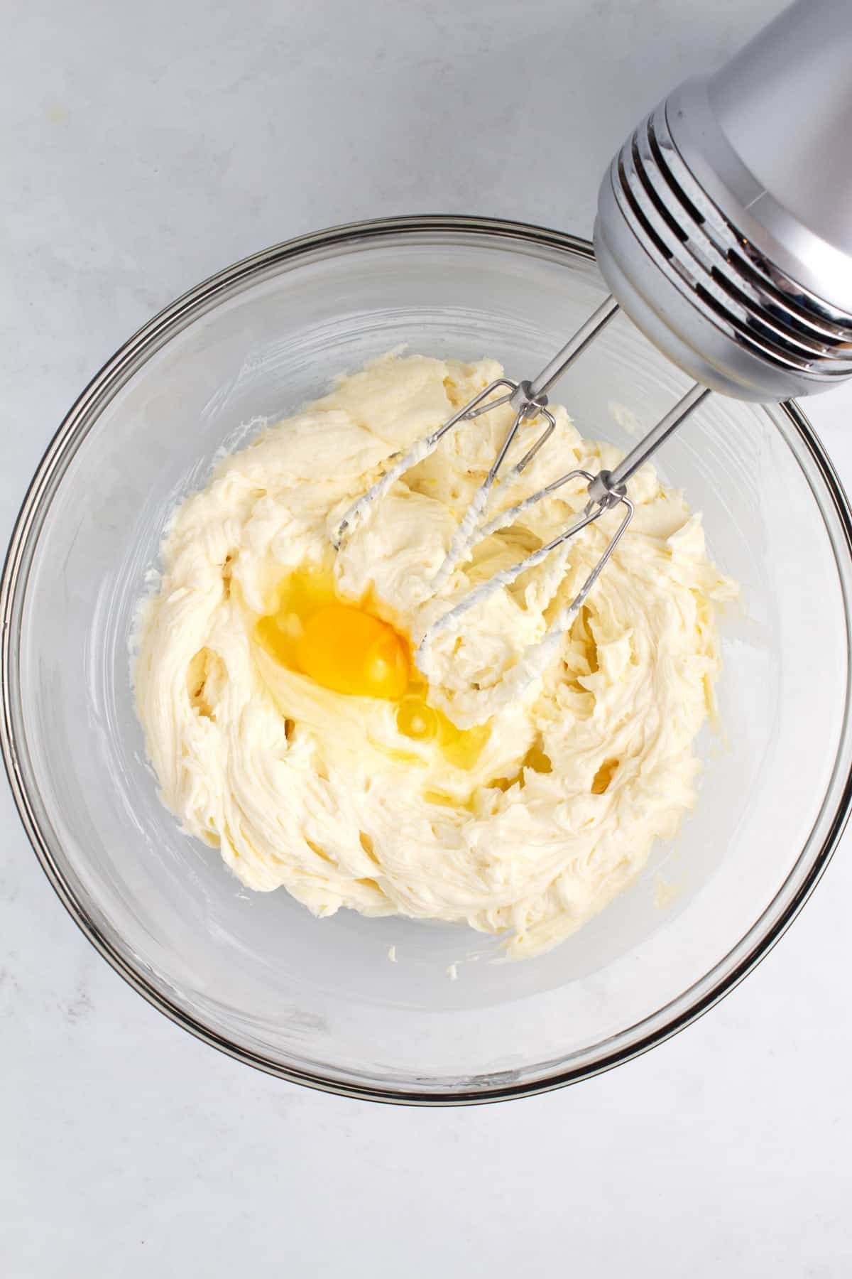 A bowl of creamy batter with an egg getting mixed in with a blender.