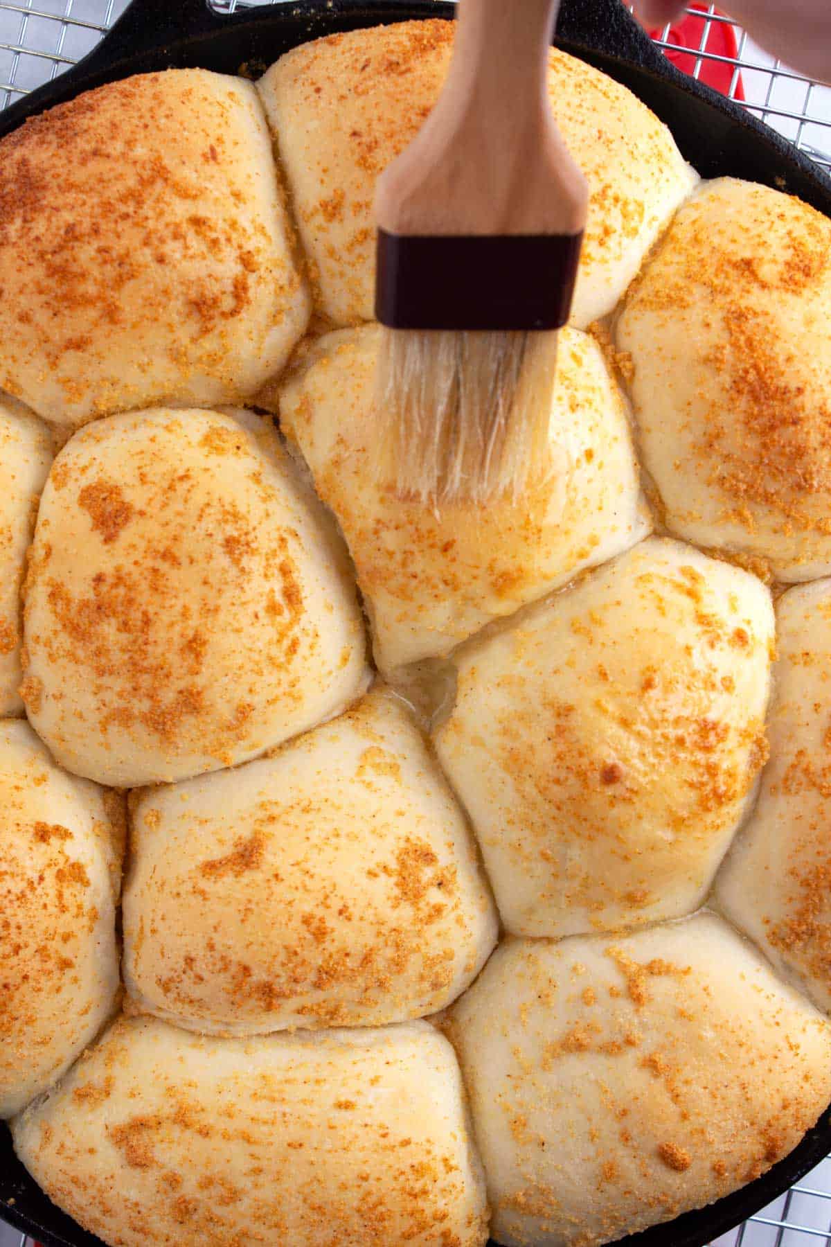 Cooked dinner rolls in a skillet getting brushed with garlic butter.