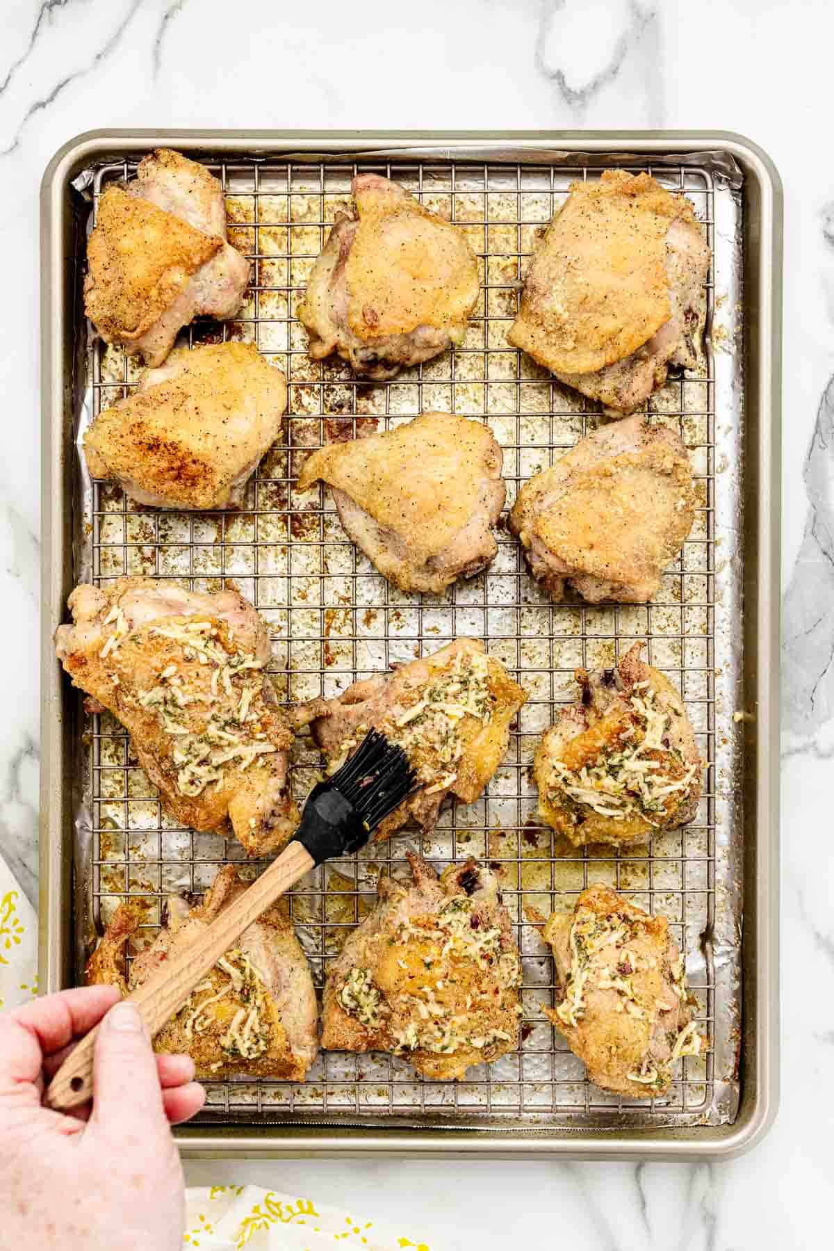 Parmesan lemon sauce being brushed onto a rack of baked chicken thighs.