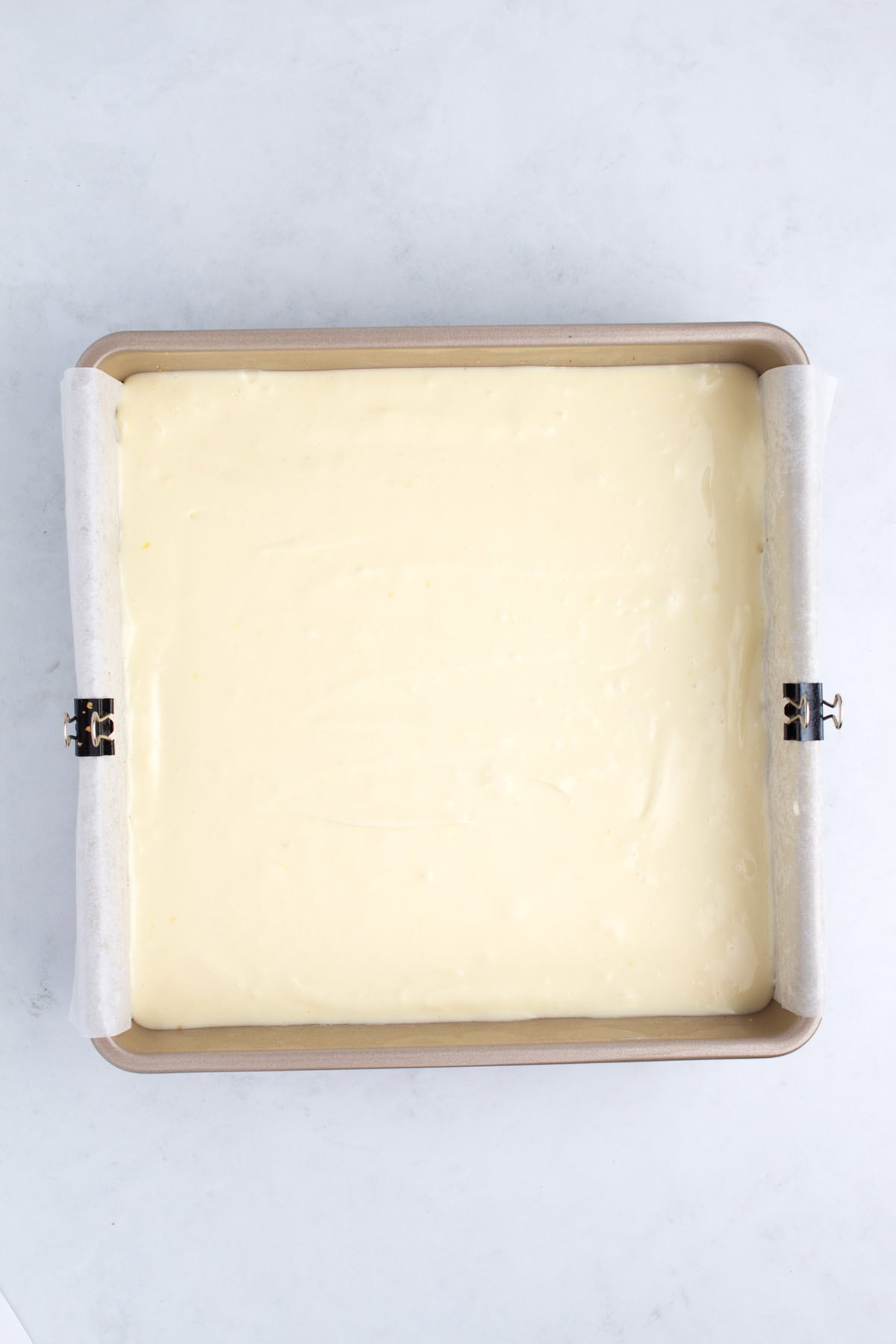A square pan filled with cheesecake batter.