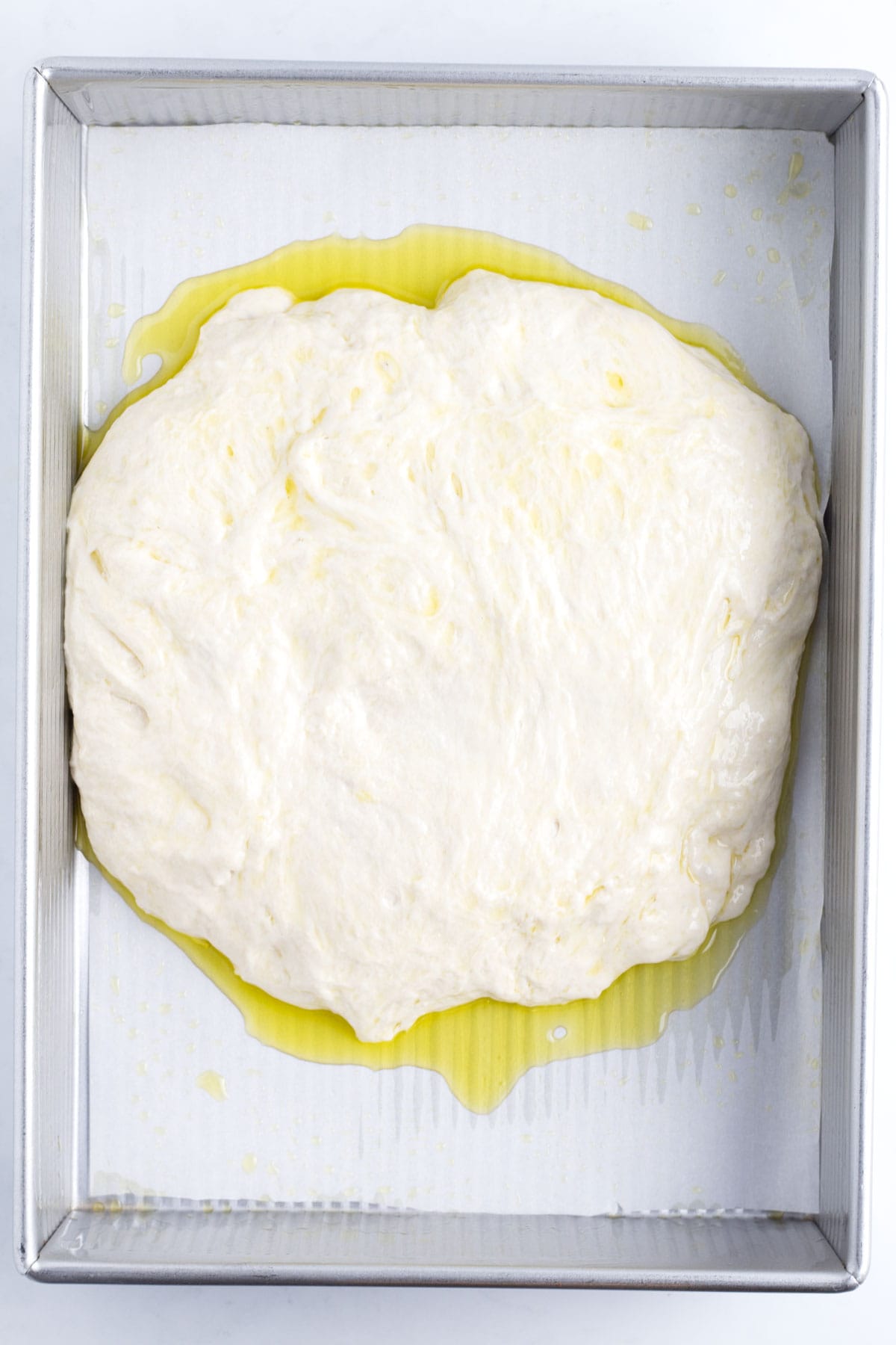 A lump of dough with oil puddled under it in a baking tray with parchment paper.