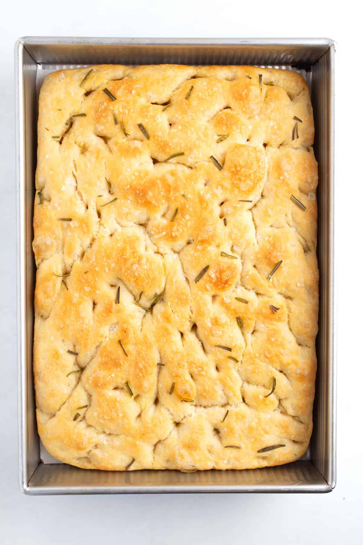 Baked golden loaf of focaccia in a metal pan.