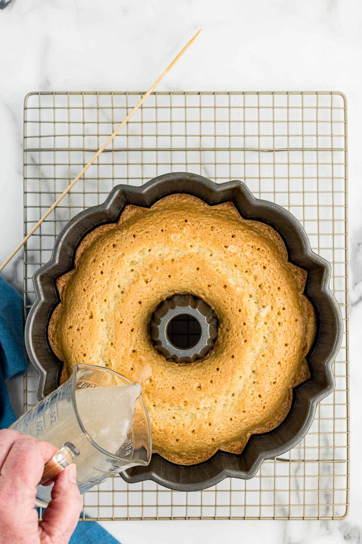 A small pitcher of coconut syrup being poured over a Bundt cake filled with holes in the top.