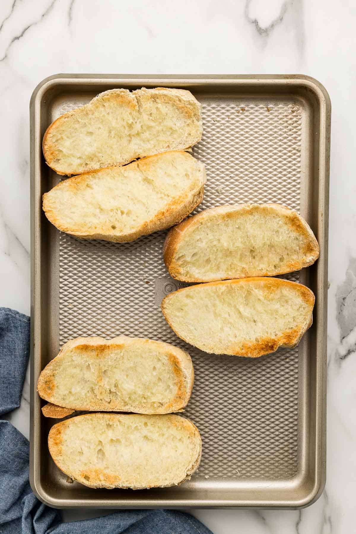 Sheet pan of sliced and baked bread on a marble counter.