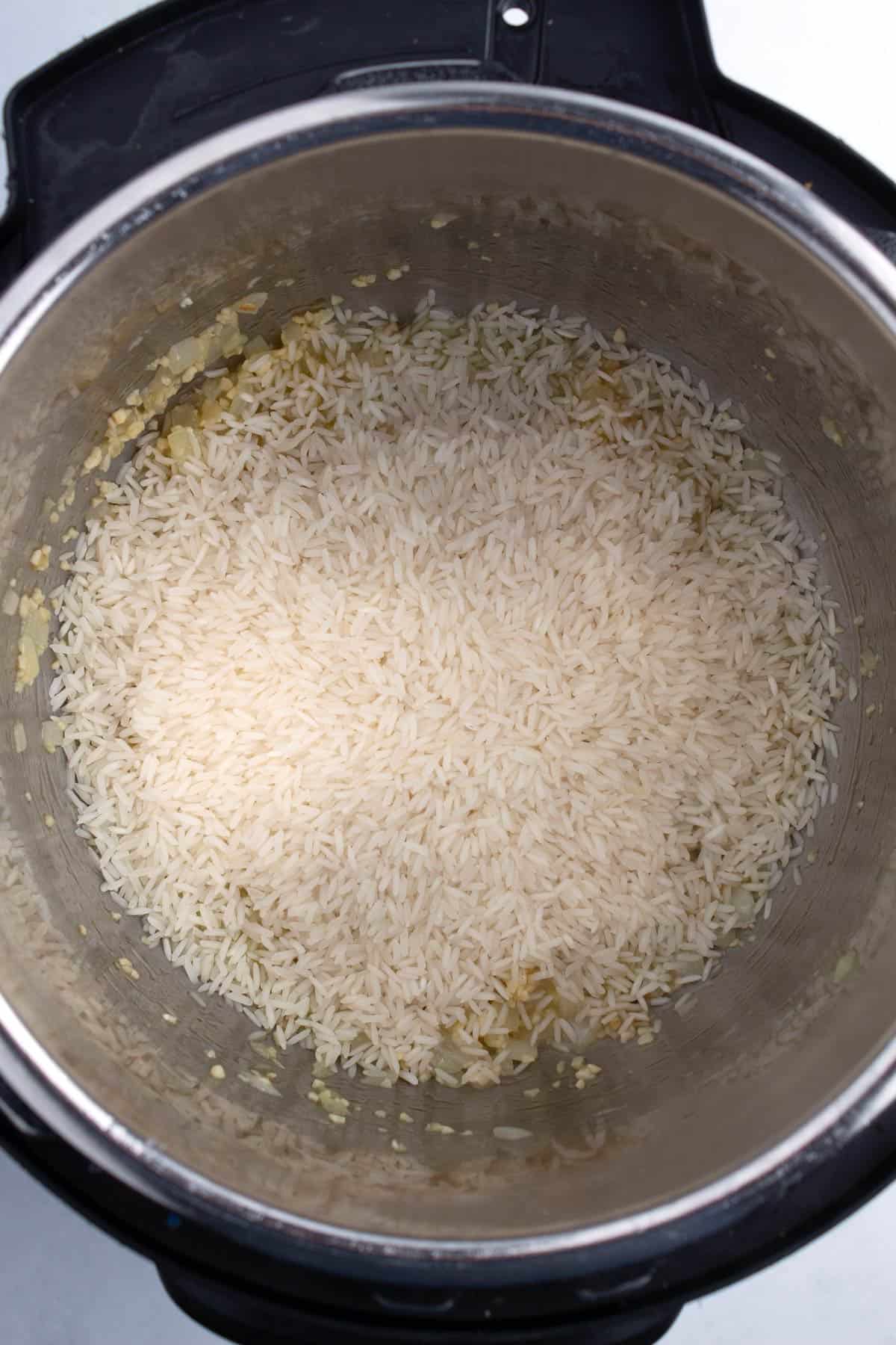 Uncooked rice poured into a stainless steel pot.