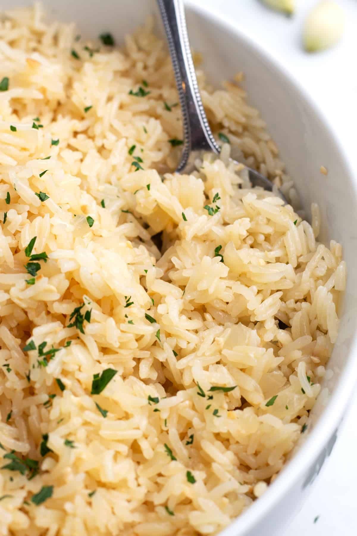 A spoon scooping a bit of garlic rice out of a white bowl.