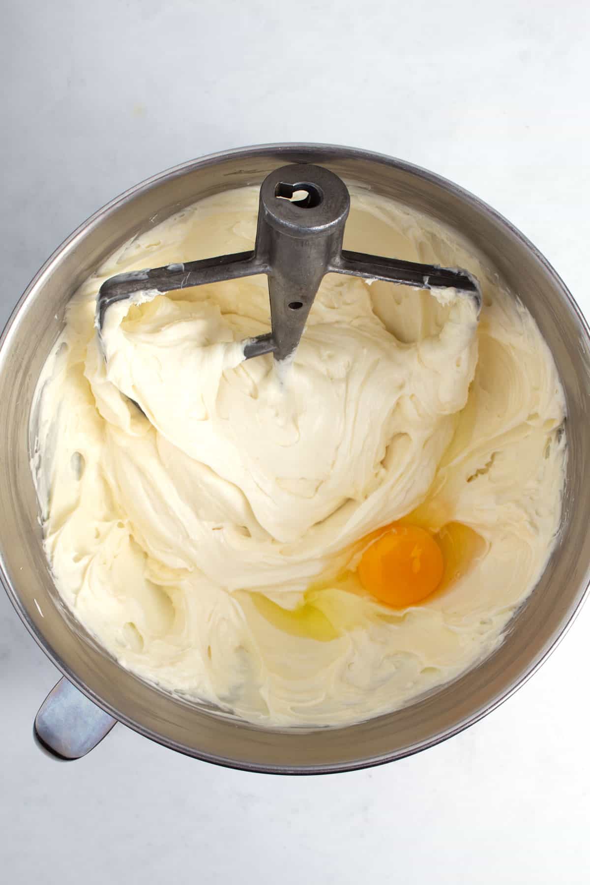 Stainless steel bowl of mixed batter and an egg with a mixing paddle in it at the top.