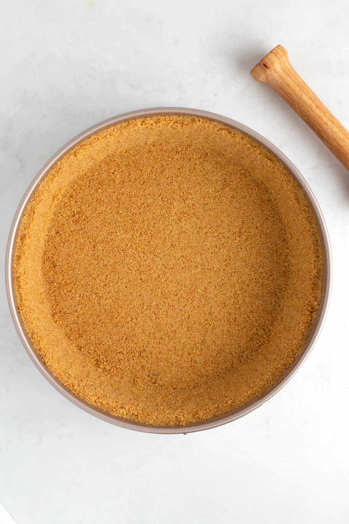 A pan of graham cracker crust with a tamper next to it.