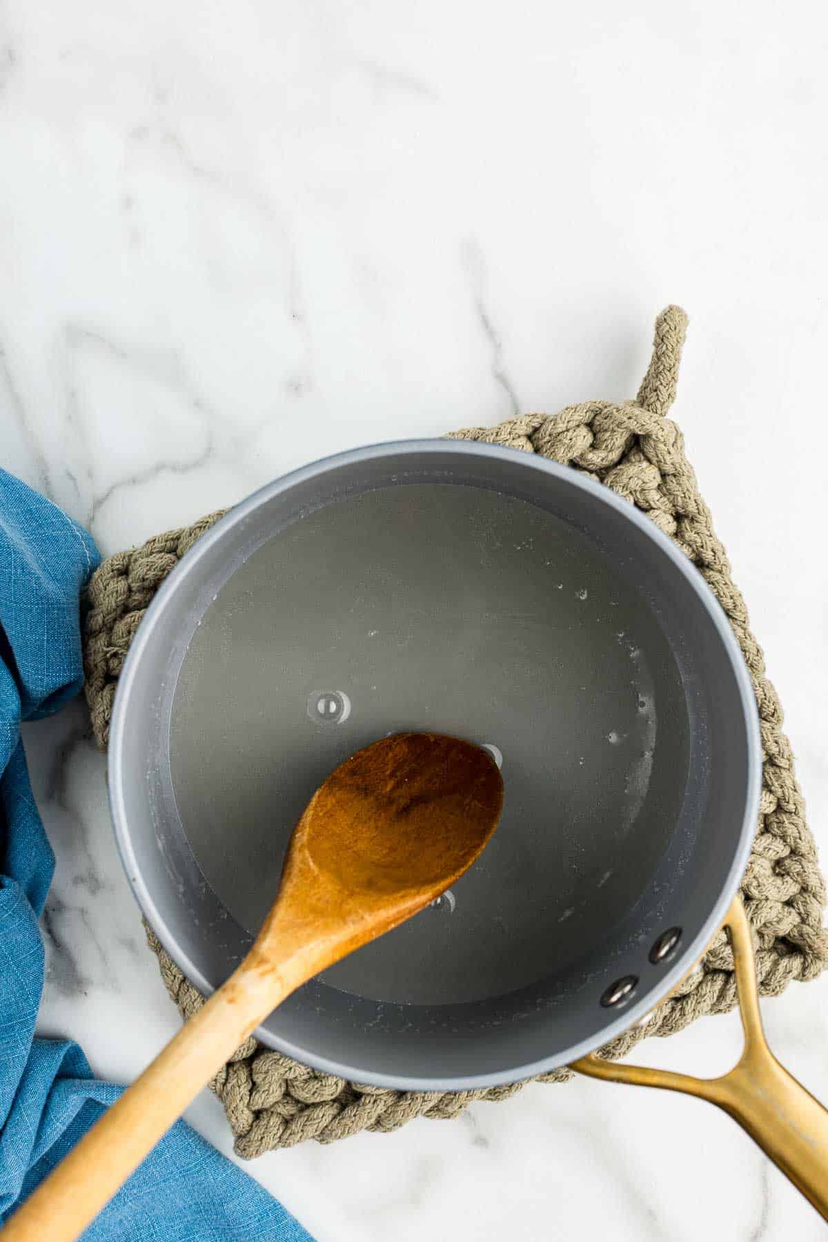 A saucepan of bubbling coconut syrup with a wooden spoon dipped in it.