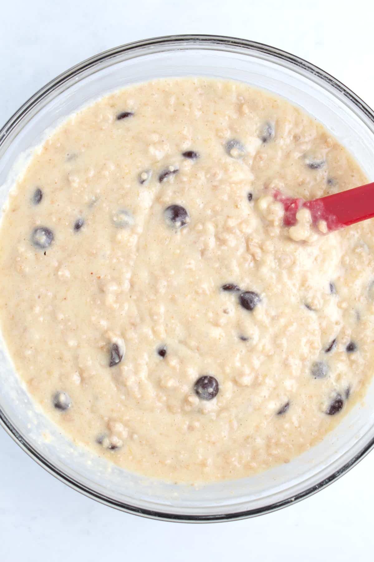 A bowl of bread dough and chocolate chips with a red spatula in it.