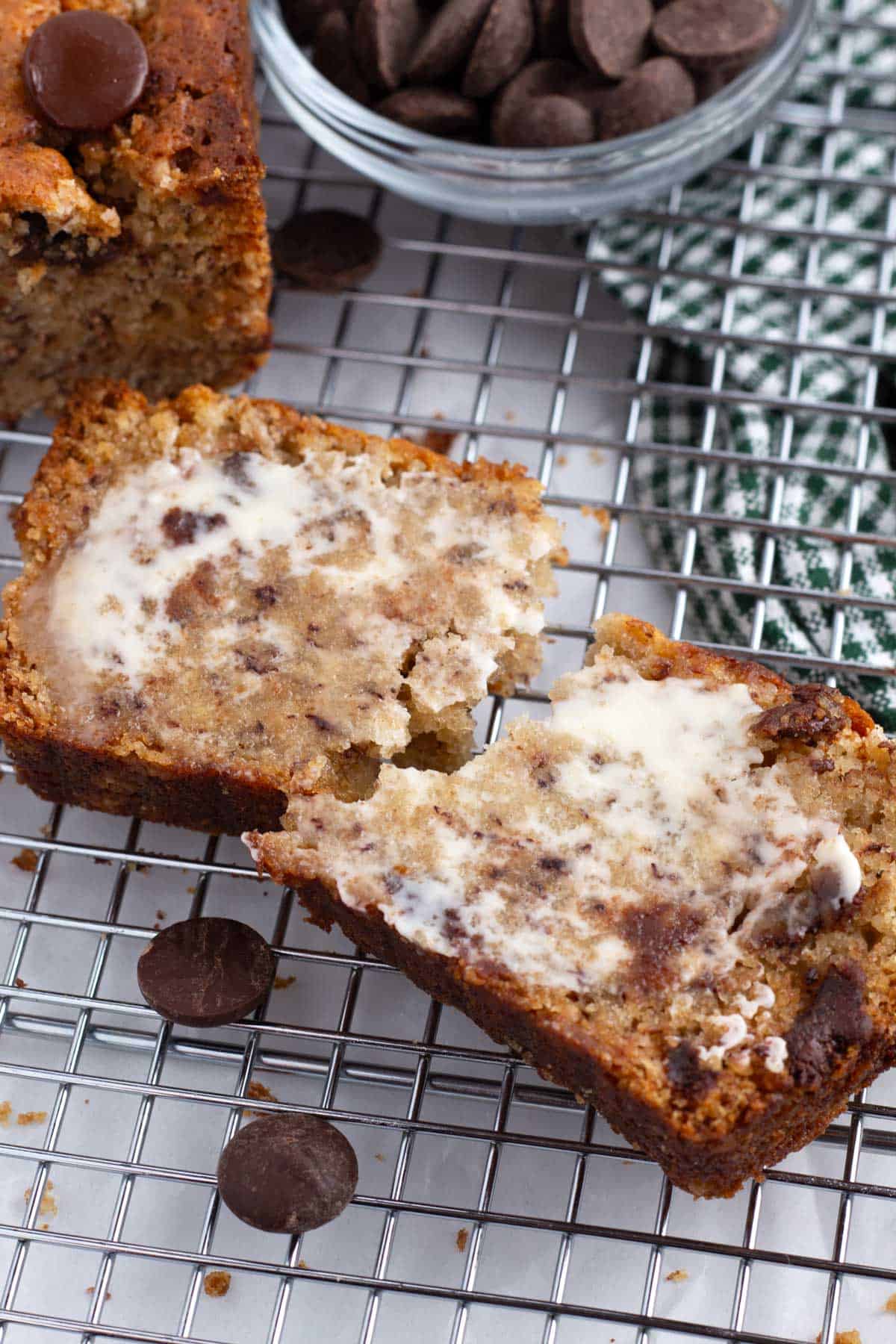 A slice of brown butter banana bread on a wire rack spread with butter next to a cut loaf.