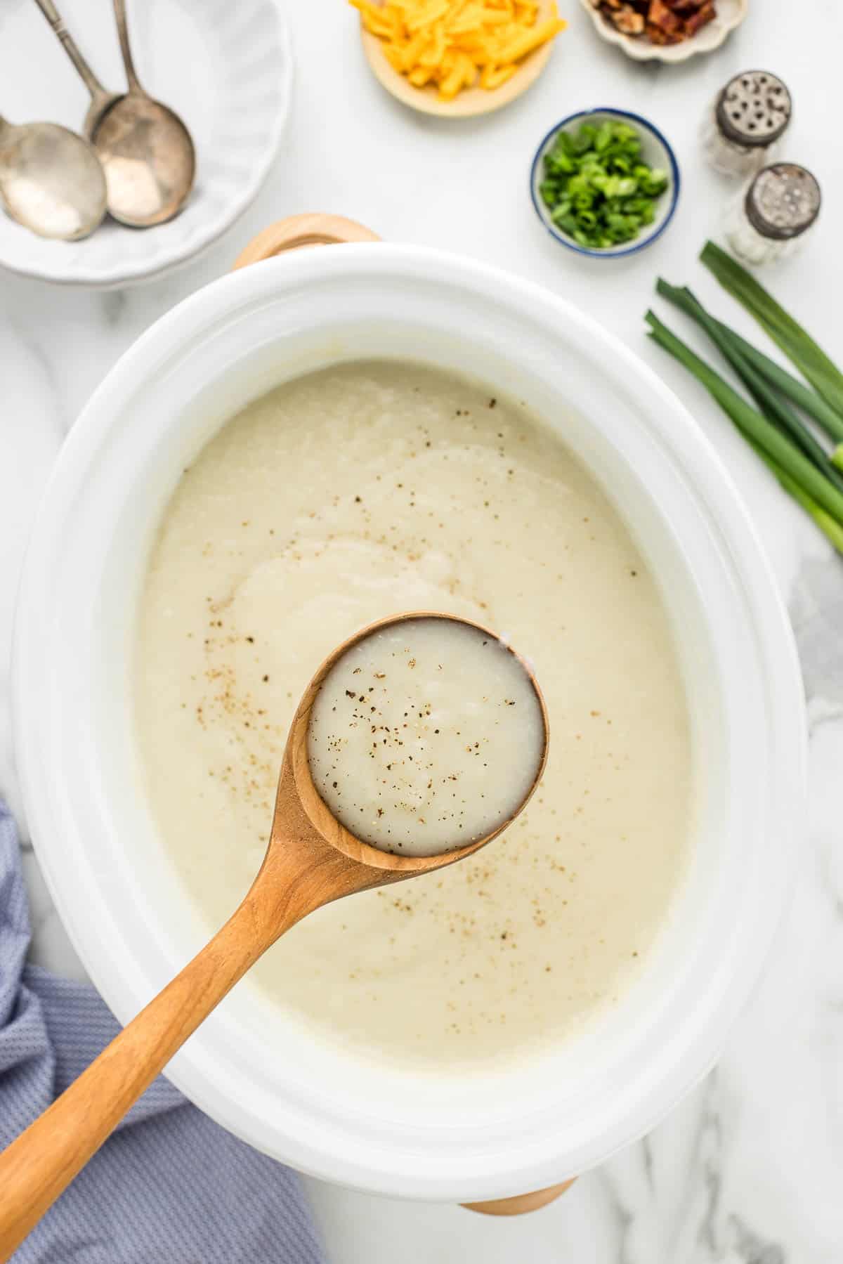 Ladle in pot of easy potato soup with empty bowls and toppings on the side.
