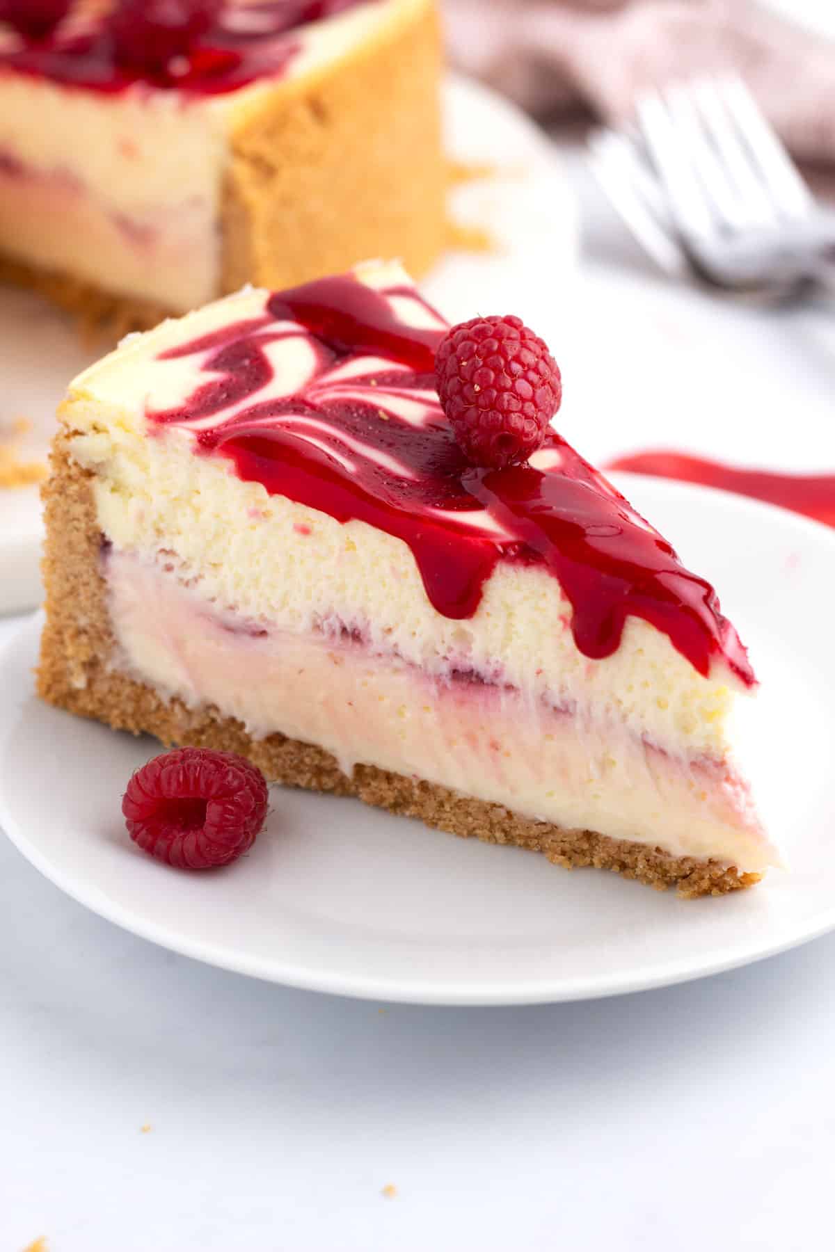A slice of raspberry cheesecake on a dessert plate in front of a cheesecake.